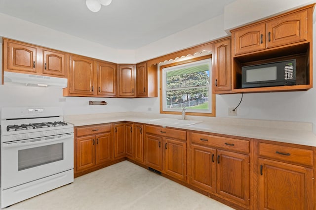 kitchen with brown cabinets, under cabinet range hood, a sink, black microwave, and white gas range oven
