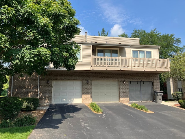 view of property featuring brick siding, driveway, a balcony, and an attached garage