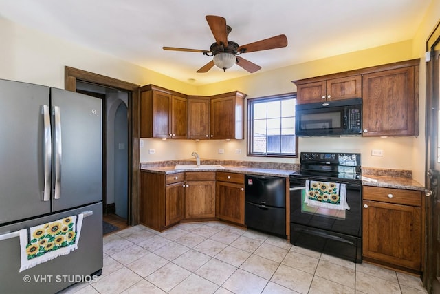 kitchen featuring light tile patterned flooring, black appliances, brown cabinetry, ceiling fan, and a sink