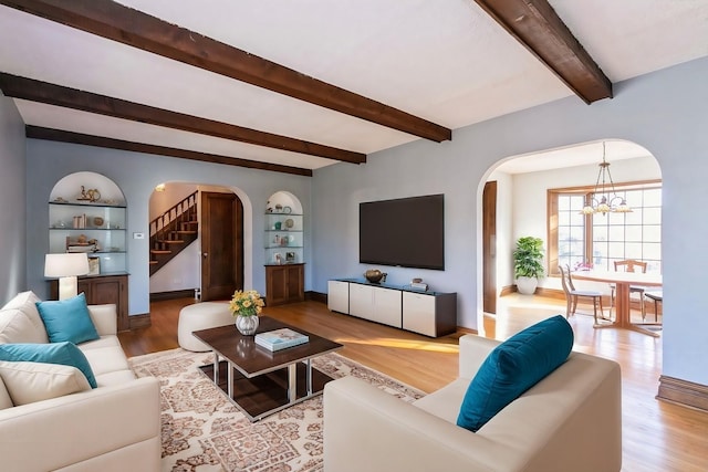 living area with arched walkways, a notable chandelier, light wood-style flooring, and beamed ceiling