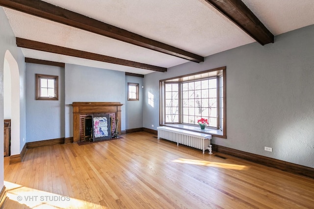 unfurnished living room with baseboards, a fireplace, beamed ceiling, light wood finished floors, and radiator