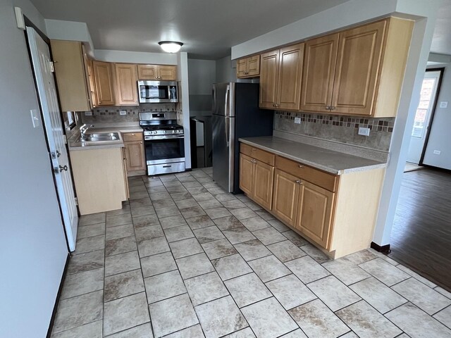 kitchen featuring light tile patterned flooring, a sink, light countertops, stainless steel appliances, and backsplash
