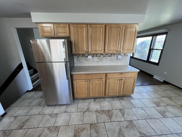kitchen with visible vents, freestanding refrigerator, light countertops, brown cabinets, and backsplash