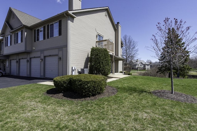 view of property exterior with a chimney, a garage, driveway, and a lawn