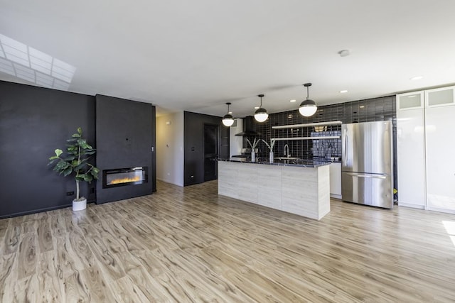 kitchen featuring light wood finished floors, modern cabinets, freestanding refrigerator, and a glass covered fireplace