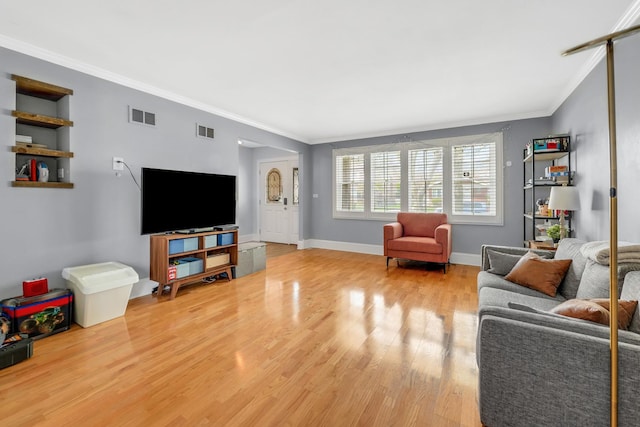 living area with baseboards, visible vents, light wood-style floors, and ornamental molding