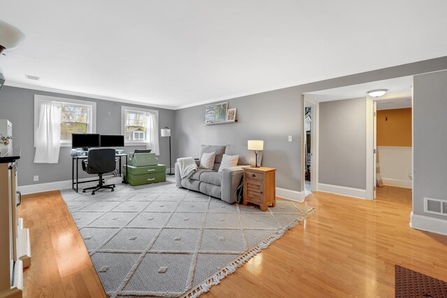 living area featuring baseboards, ornamental molding, light wood finished floors, and visible vents
