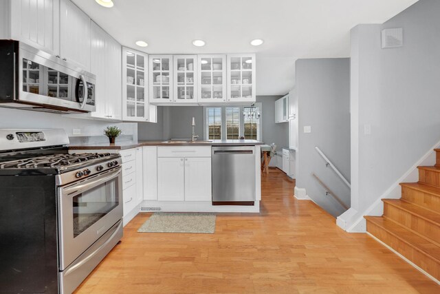 kitchen with a sink, white cabinetry, a peninsula, appliances with stainless steel finishes, and recessed lighting