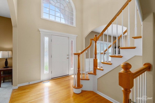 foyer entrance featuring a high ceiling, wood finished floors, stairs, arched walkways, and baseboards