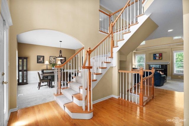 stairway with arched walkways, wood finished floors, a towering ceiling, baseboards, and carpet floors