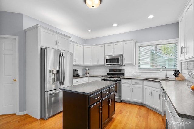 kitchen with appliances with stainless steel finishes, a sink, backsplash, a kitchen island, and light wood finished floors