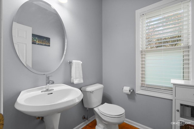 half bath featuring toilet, baseboards, a sink, and wood finished floors
