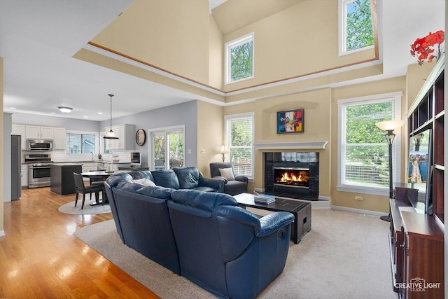 living area featuring a fireplace, a high ceiling, baseboards, light wood-type flooring, and recessed lighting