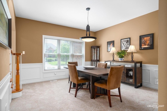 dining space with a wainscoted wall, light carpet, and a decorative wall