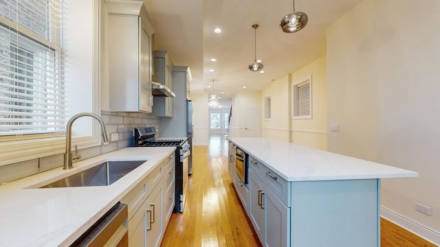 kitchen with gray cabinetry, appliances with stainless steel finishes, light wood finished floors, a sink, and hanging light fixtures