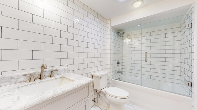 full bathroom featuring toilet, vanity, combined bath / shower with glass door, and tile walls