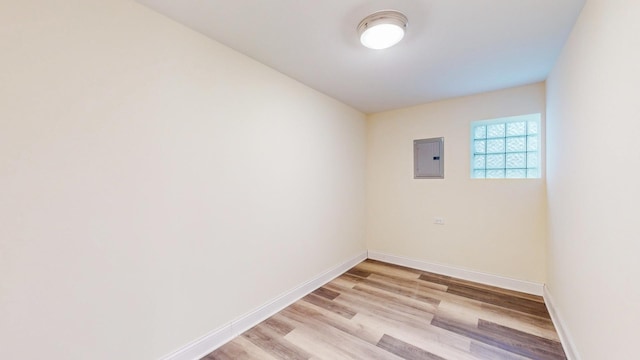 empty room with light wood-type flooring, baseboards, and electric panel