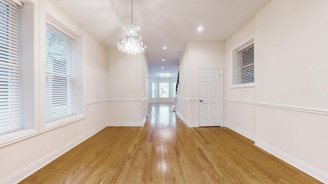 corridor featuring light wood finished floors, baseboards, an inviting chandelier, and recessed lighting