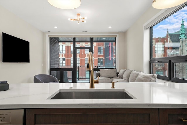kitchen with light stone countertops, a sink, dishwashing machine, and a notable chandelier