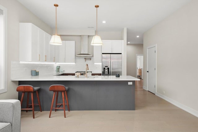 kitchen featuring tasteful backsplash, a kitchen breakfast bar, wall chimney range hood, a peninsula, and stainless steel refrigerator with ice dispenser