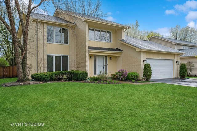traditional home featuring a front lawn, fence, roof with shingles, an attached garage, and driveway