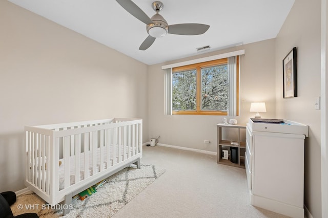 bedroom with ceiling fan, light colored carpet, a crib, baseboards, and visible vents