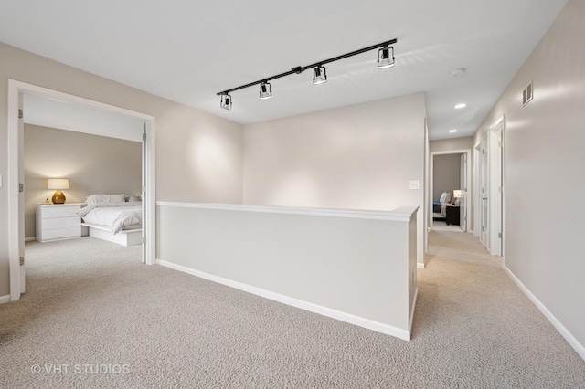 hall with baseboards, rail lighting, visible vents, and light carpet