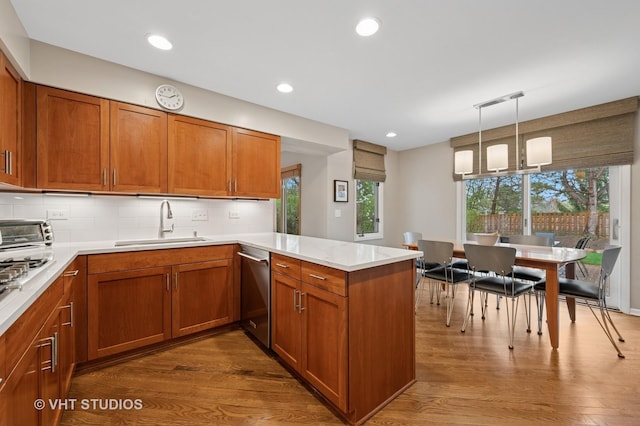 kitchen with a sink, stainless steel dishwasher, brown cabinets, and a peninsula