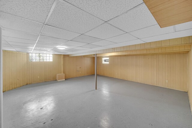below grade area with baseboards, wood walls, and a drop ceiling