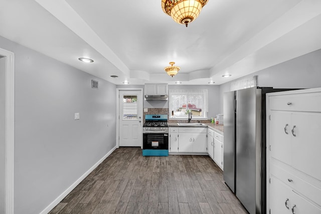 kitchen featuring wood finished floors, gas range, a tray ceiling, white cabinets, and under cabinet range hood