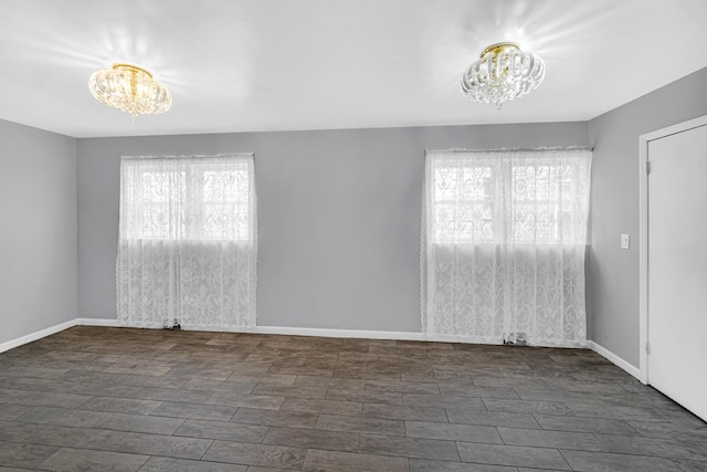 spare room featuring a wealth of natural light, baseboards, dark wood-style flooring, and an inviting chandelier