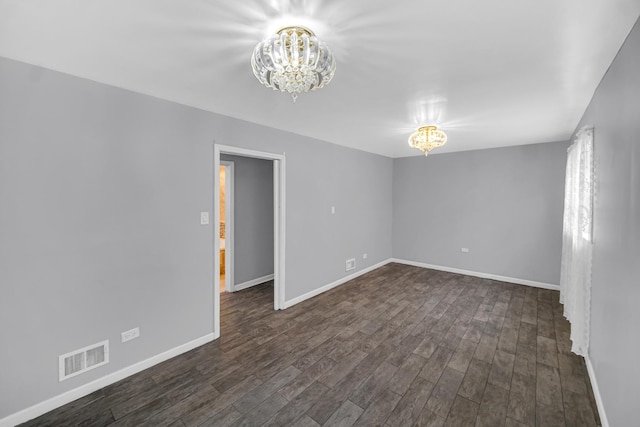 empty room featuring dark wood finished floors, an inviting chandelier, visible vents, and baseboards