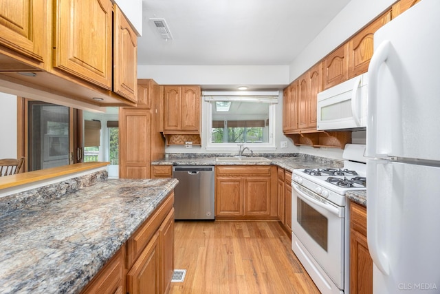kitchen with white appliances, a sink, light wood-style floors, and light stone countertops