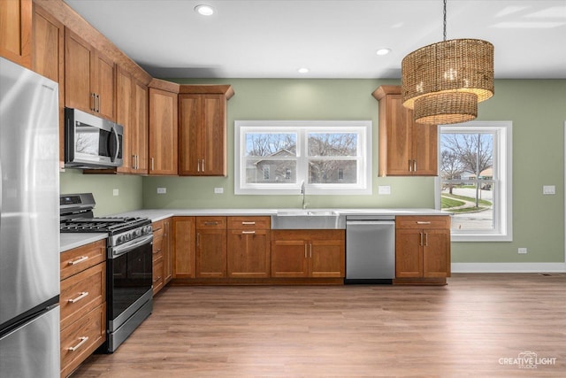 kitchen with light wood-type flooring, brown cabinetry, stainless steel appliances, and a sink