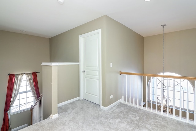 hall with an upstairs landing, baseboards, and carpet floors