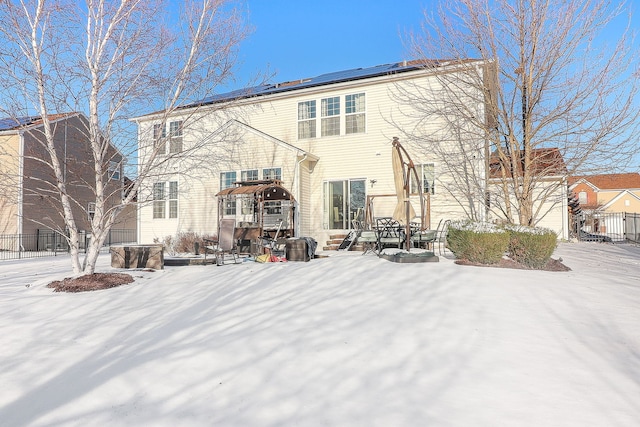 snow covered rear of property with fence and solar panels