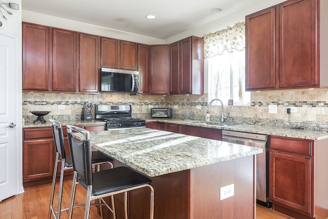 kitchen featuring a breakfast bar, a center island, light stone countertops, appliances with stainless steel finishes, and a sink