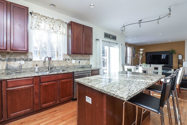 kitchen featuring light stone countertops, light wood-style floors, a kitchen bar, stainless steel dishwasher, and a sink