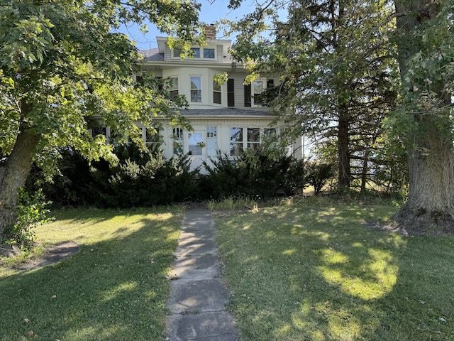 view of front of home featuring a front yard, a chimney, and a shingled roof
