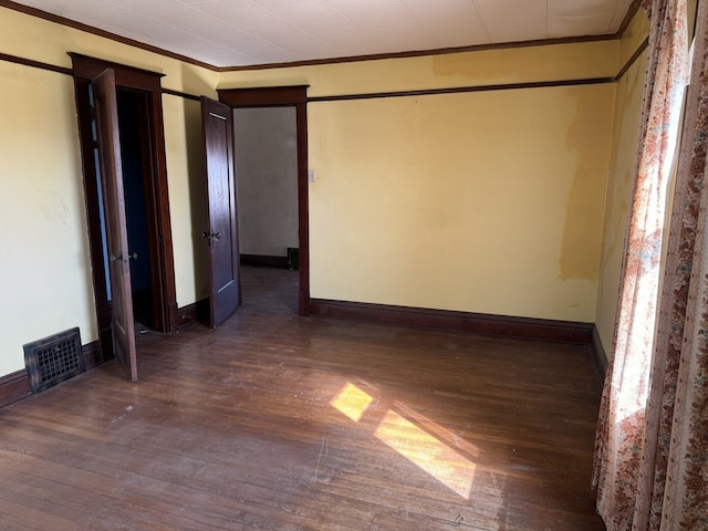 unfurnished room featuring visible vents, baseboards, crown molding, and wood finished floors