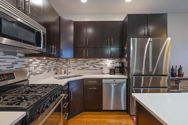kitchen featuring light wood-type flooring, appliances with stainless steel finishes, light countertops, a sink, and decorative backsplash