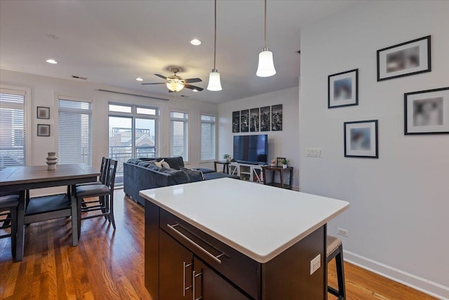 kitchen featuring light countertops, ceiling fan, a kitchen breakfast bar, wood finished floors, and pendant lighting