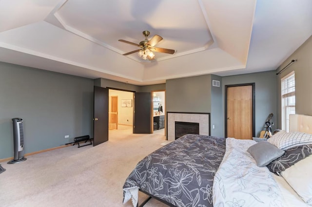 carpeted bedroom with a tray ceiling, baseboards, a tiled fireplace, and visible vents