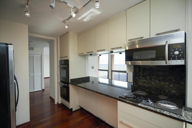 kitchen with black appliances, dark wood-style flooring, tasteful backsplash, dark stone countertops, and rail lighting