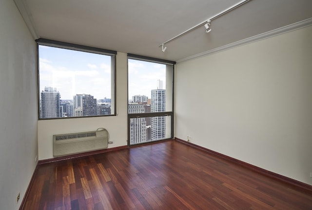 empty room with rail lighting, plenty of natural light, wood finished floors, and a wall unit AC