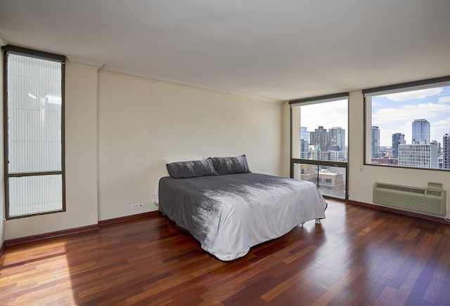bedroom with a skyline view, wood finished floors, a wall mounted air conditioner, crown molding, and baseboards