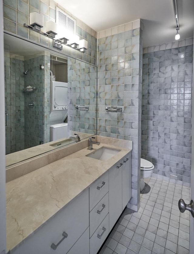 full bathroom featuring tile walls, stacked washer / drying machine, tile patterned flooring, toilet, and a shower stall