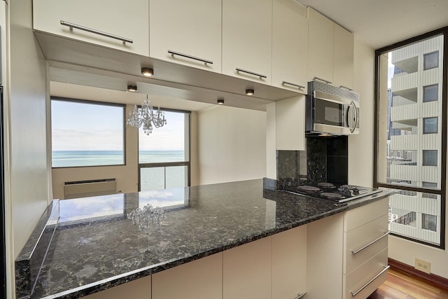kitchen with stainless steel microwave, dark stone counters, a chandelier, wood finished floors, and black electric cooktop