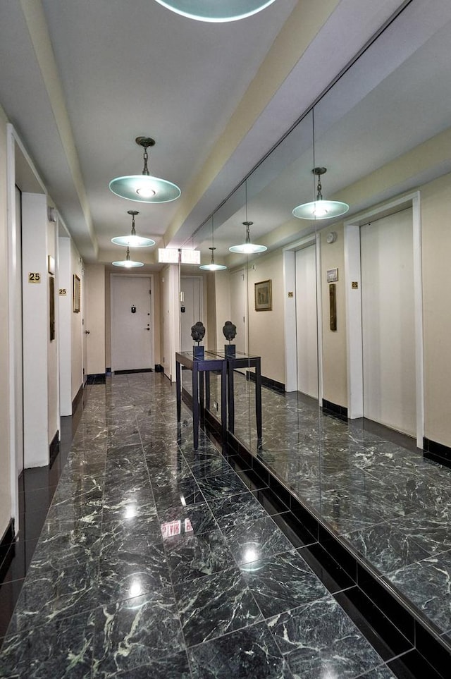 hallway featuring baseboards, elevator, marble tiled floors, and a raised ceiling