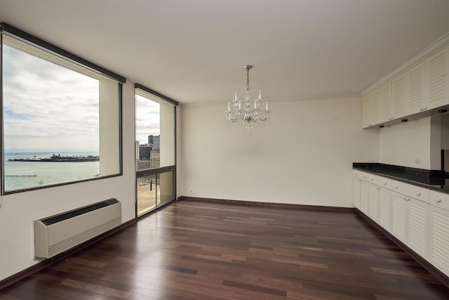 unfurnished dining area featuring dark wood-type flooring, a chandelier, baseboards, and ornamental molding